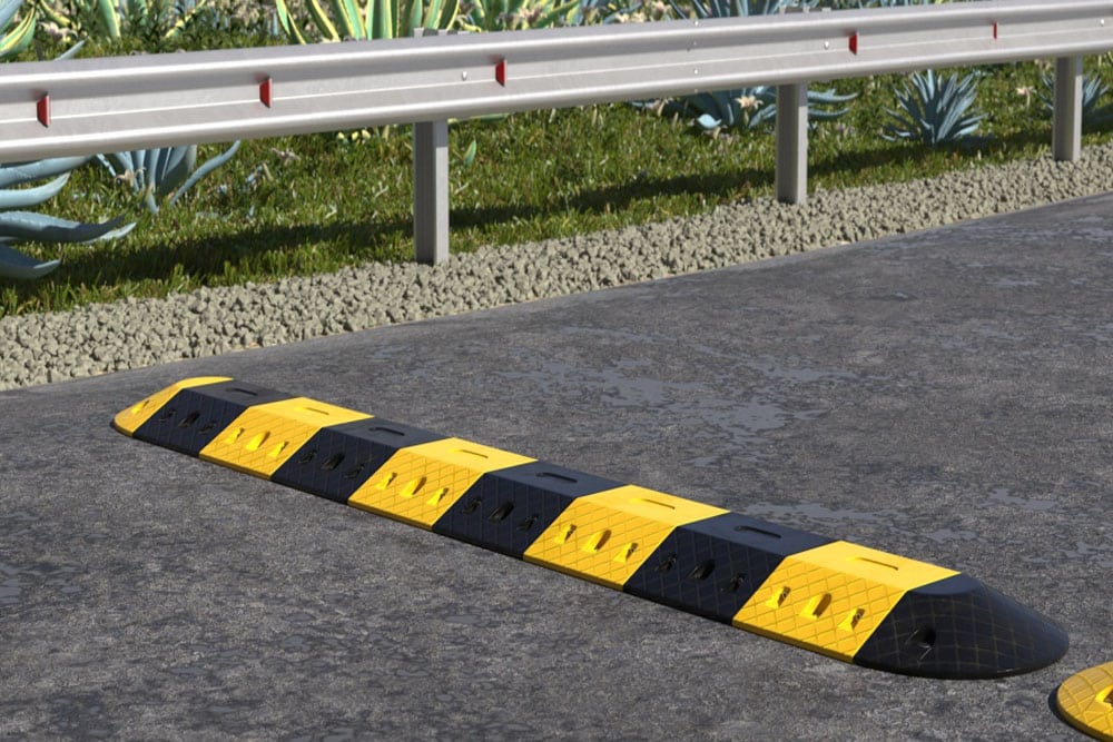 Yellow and black rubber speed hump beside a roadside guardrail