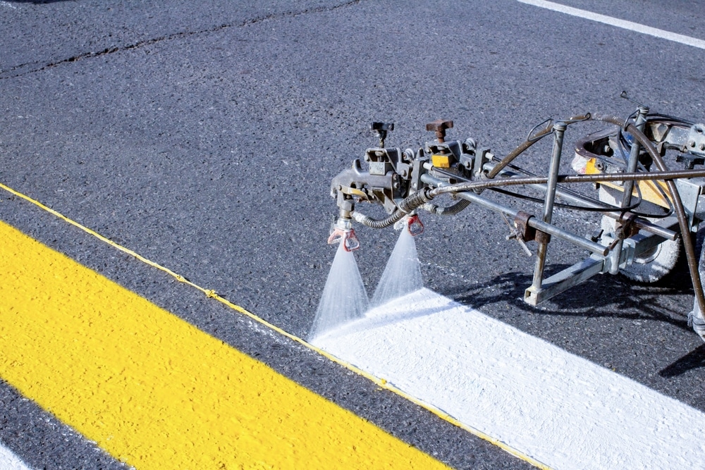Line marking machine applying white road markings beside a yellow line