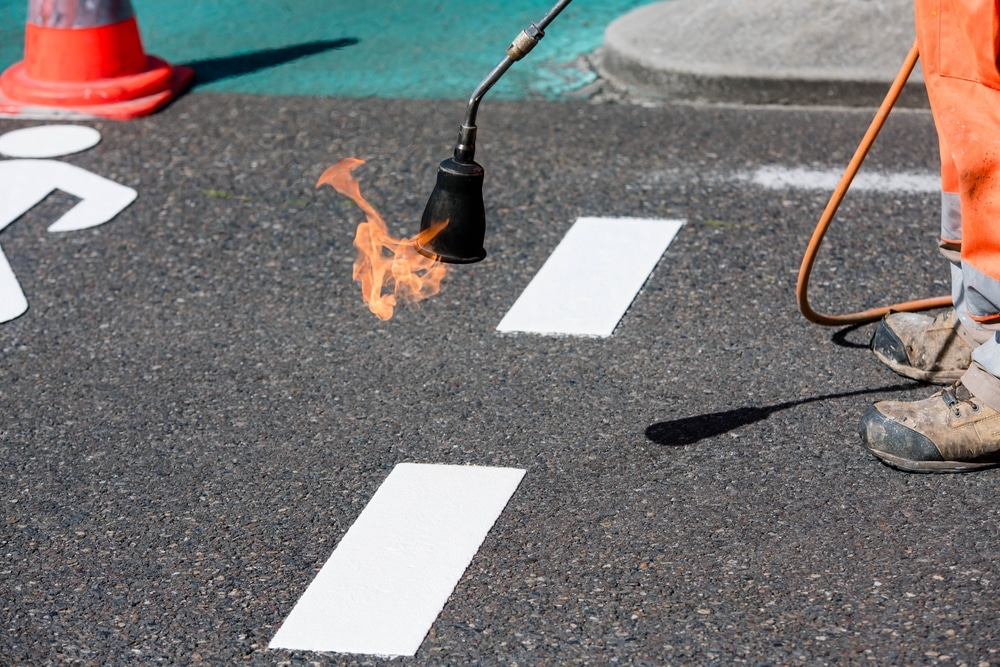 Road worker heat-applying white thermoplastic pavement markings