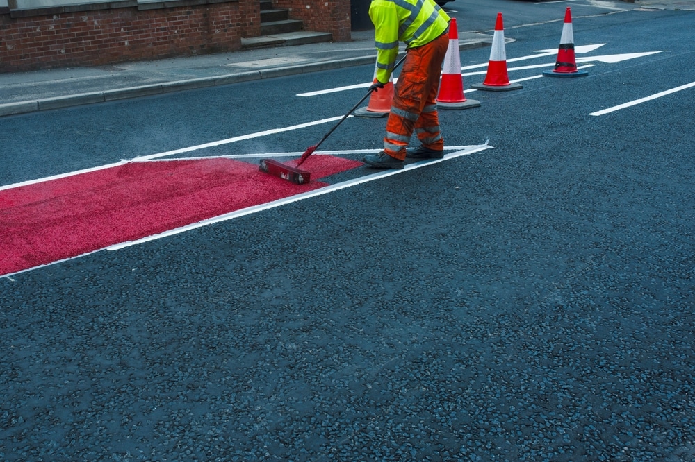 Road worker applying red safety markings to an asphalt road